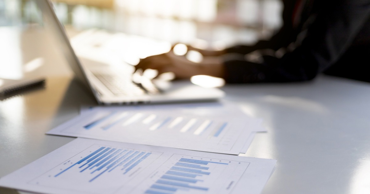 Blurry figure working at laptop with financial charts in the foreground